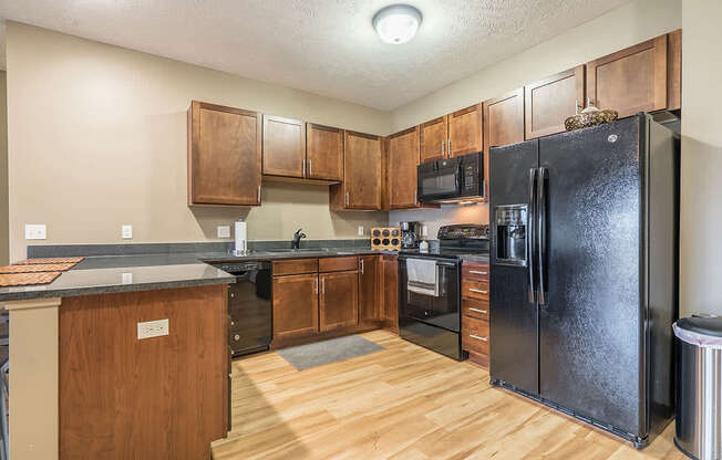 A kitchen with a black refrigerator and warm, medium brown wooden cabinets.