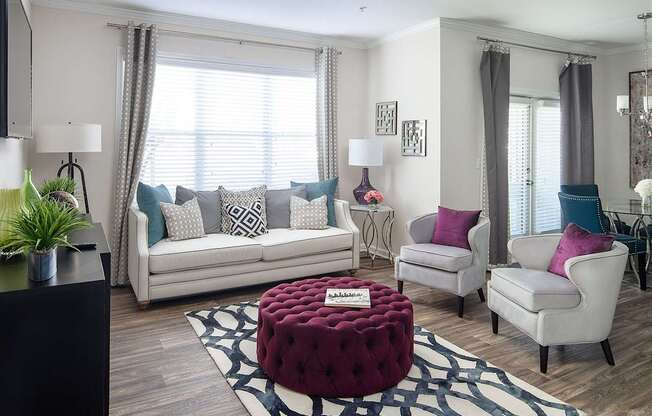 A living room with a white couch, two chairs, and a red ottoman.