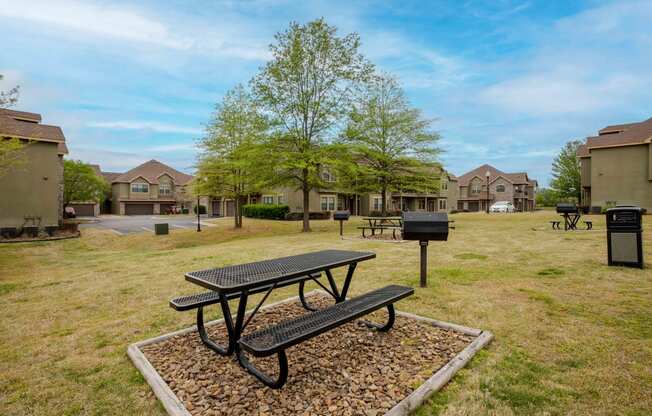 a picnic table with a grill in a grassy area with houses in the background