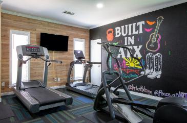 A gym with treadmills and a wall with a guitar and the words "Built in Ax" on it.