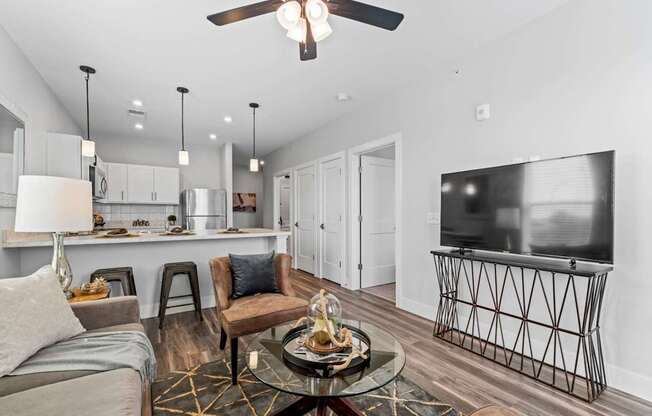 A modern living room with a grey sofa, a glass coffee table, and a television on a stand.
