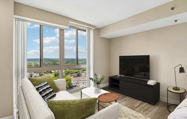 A living room with a couch, a chair, a coffee table, a television, and a window with a view of the city.