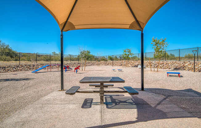 A playground with a picnic table and a canopy is set in a sunny, open area.