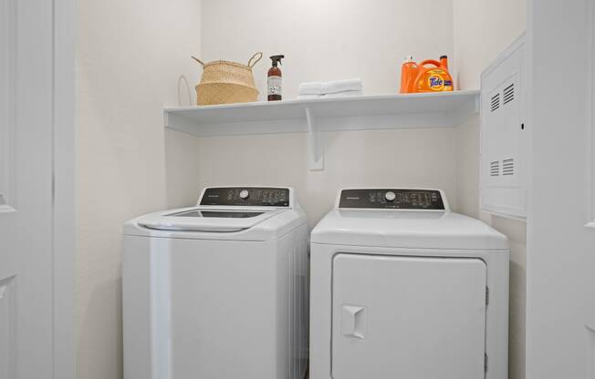 a washer and dryer in a white laundry room with a shelf above it