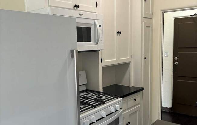 a small kitchen with white cabinets and a stove and microwave