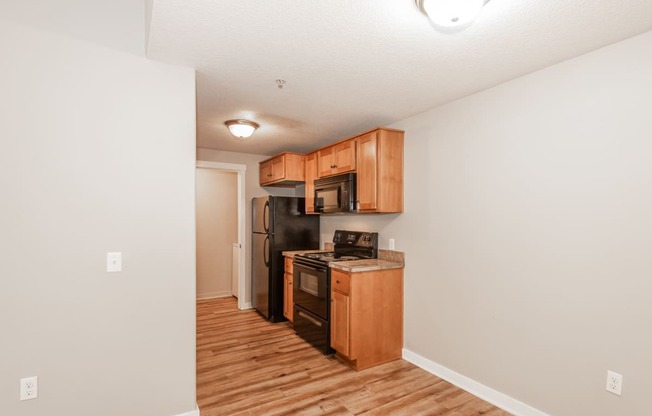 a kitchen with wood flooring and wooden cabinets and a black refrigerator