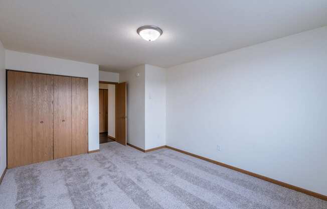 a bedroom with carpet and a door to a hallway. Moorhead, MN South Park Apartments