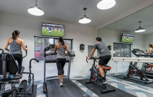 A gym with people exercising and a TV screen showing a soccer game.