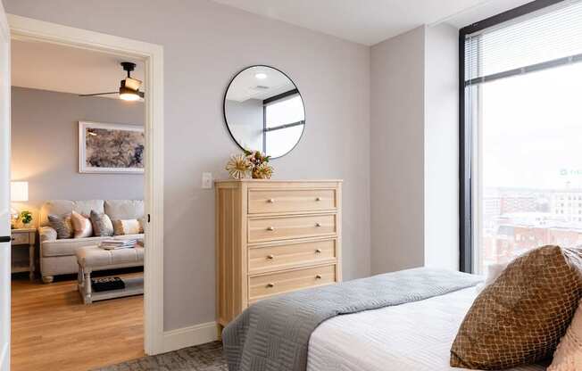 A bedroom with a bed, dresser, and a round mirror on the wall.