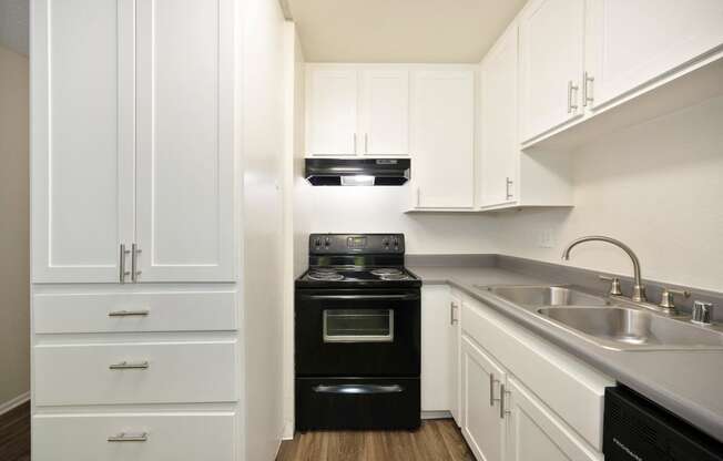 a studio apartment kitchen with white cabinets and a black oven and sink