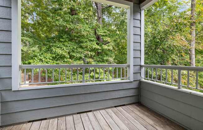 A wooden deck with a railing and a view of a green forest.