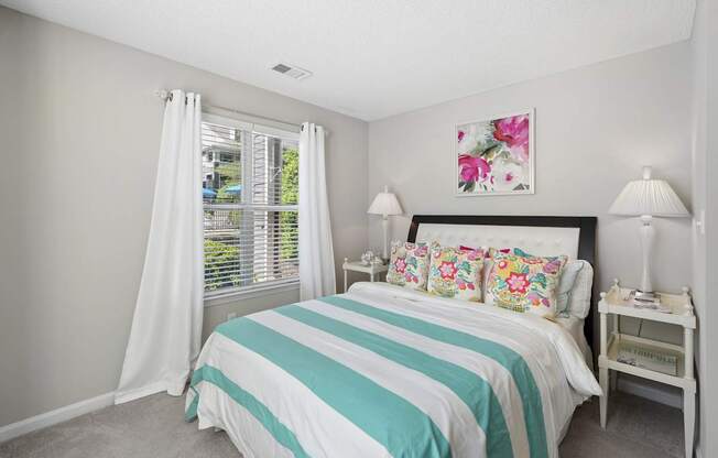 A bedroom with a bed, nightstand, and window with white curtains.
