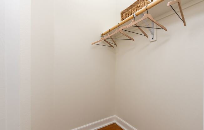 a walk in closet with white walls and shelves and a basket on a rack