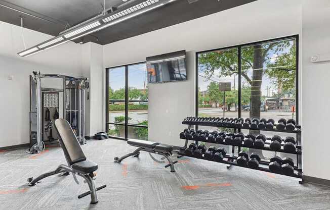 A gym with a bench, weights, and a television.