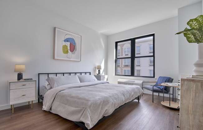 Cozy bedroom at The Mint Rahway featuring a large window, modern artwork, and comfortable furnishings, perfect for studio apartments close to the Rahway Train Station.