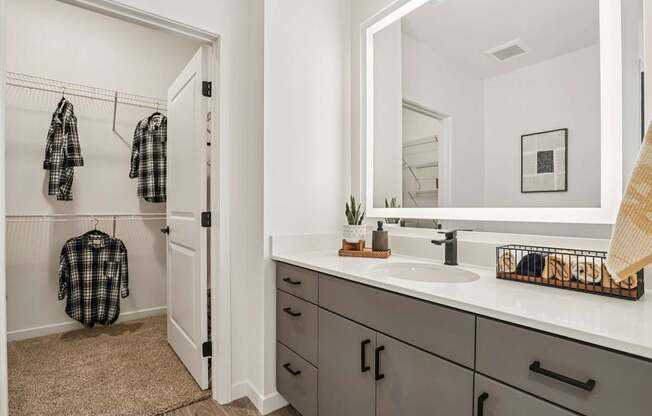 A bathroom with a sink, mirror, and a checkered shirt hanging up.