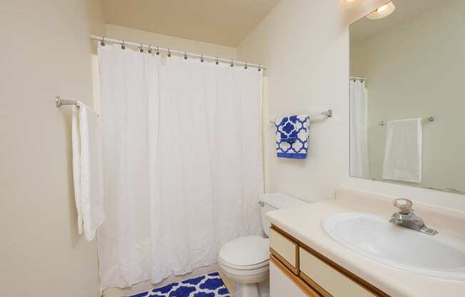 a bathroom with a white shower curtain and a sink and a toilet. Fargo, ND Twin Parks Apartments.