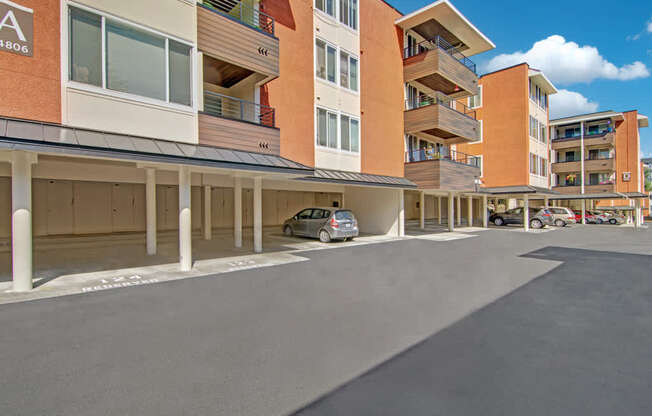 A well-maintained exterior here at Watercrest with covered parking spaces beneath the apartment building, featuring private balconies above and a clean paved driveway, creating a convenient and welcoming residential setting.