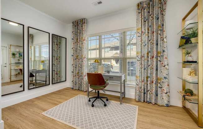 A room with a desk and a chair in front of a window with curtains.