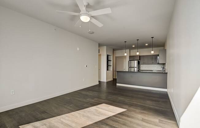 an empty living room with a ceiling fan and a kitchen in the background
