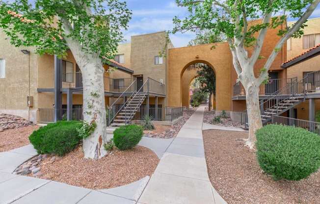 A courtyard with a pathway, trees, and bushes in front of apartment buildings.
