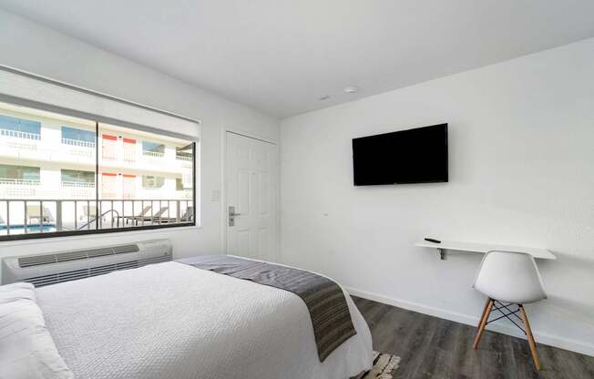 A bedroom with a bed, chair, and a flat screen TV mounted on the wall.