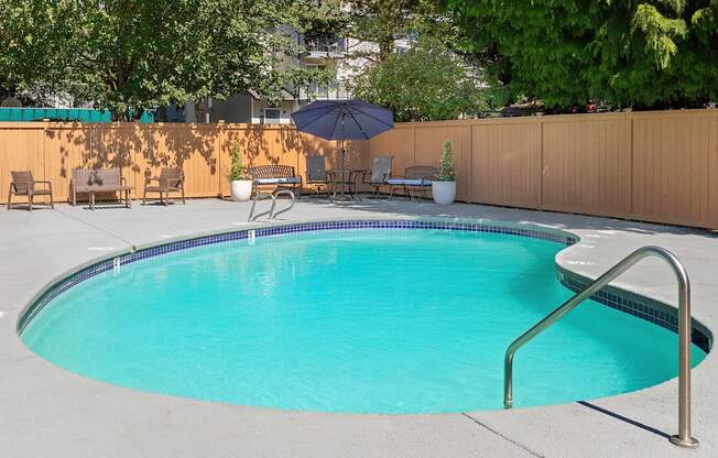 Fenced pool area with patio seating and an umbrella at Casa Blanca Apartment Homes, Everett, WA, 98204