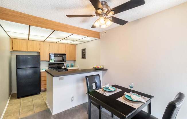 A kitchen with a black fridge and a black dining table with two chairs.