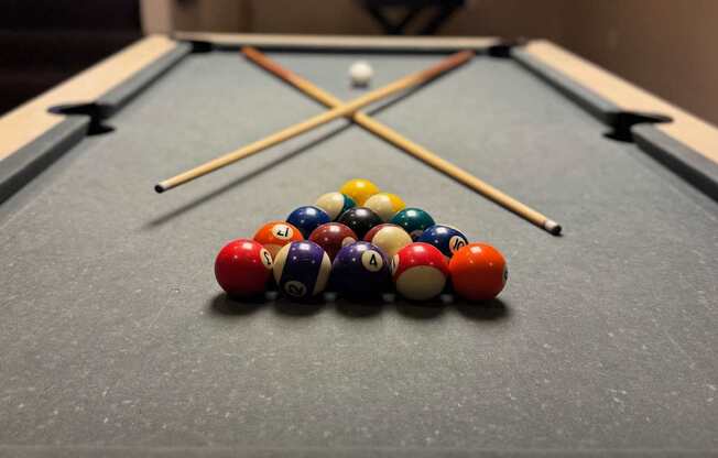 A pool table with a variety of balls and two cues.