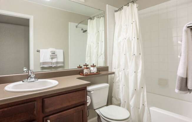 guest bathroom with wooden cabinets, large mirror, sink, toilet and tub/shower