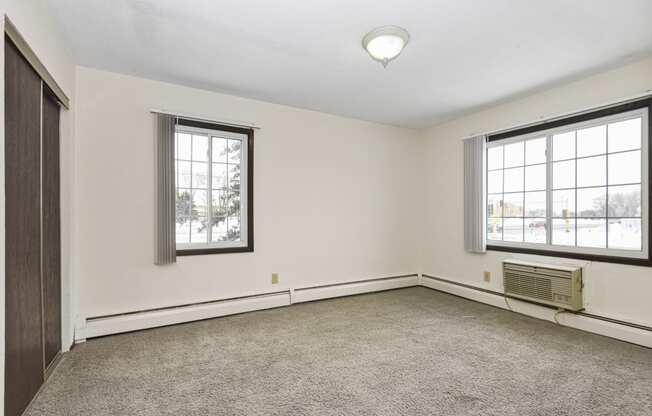 a bedroom of an empty house with carpet and two windows. Fridley, MN Georgetown on the River Apartments