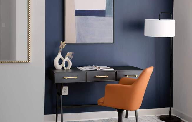 A desk with a chair and a lamp in front of a blue wall.