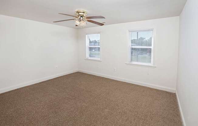 A room with a ceiling fan and two windows.