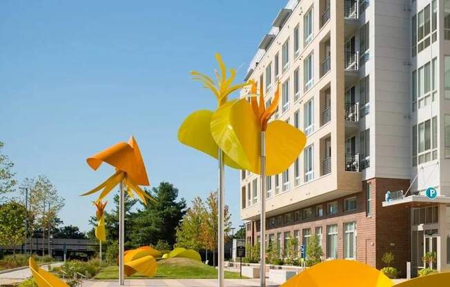 A yellow sculpture of a flower is in front of a building.