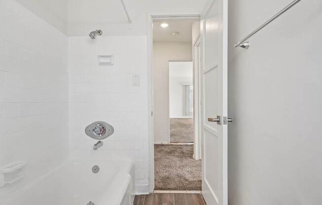A white bathroom with a tub and a doorway leading to another room.