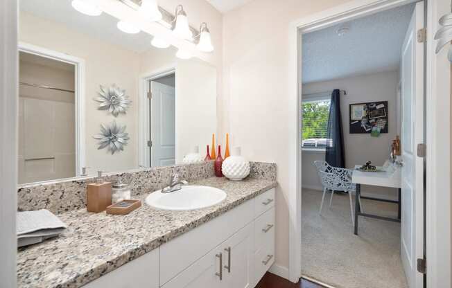 a bathroom with a sink and a mirror and a door to a bedroom