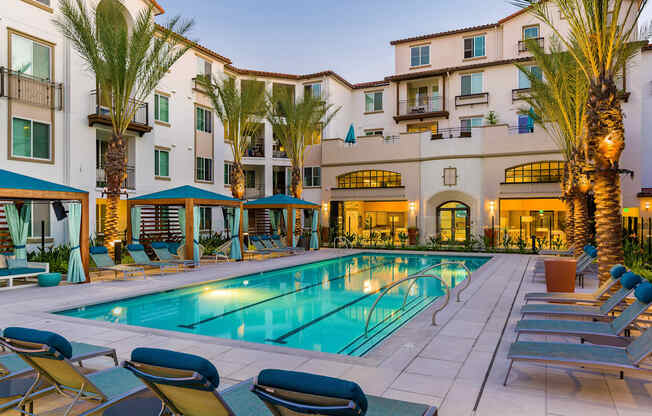 A pool surrounded by lounge chairs and palm trees.