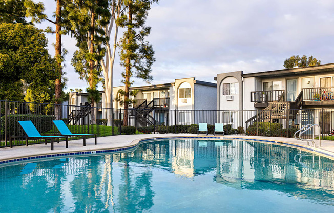 A swimming pool in front of apartment buildings with trees in the background.