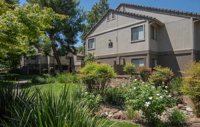 An apartment building with a grey exterior and a garden in front at Zinfandel Village Apartments, California, 95670
