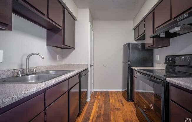 an empty kitchen with black appliances and wood flooring in an apartment