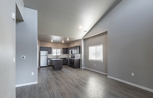 an empty living room with a kitchen in the background