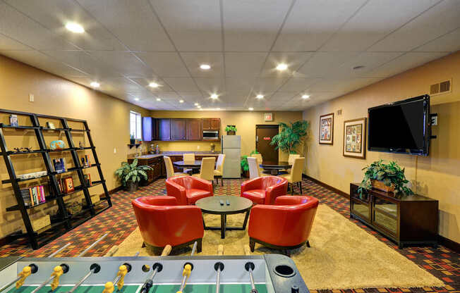 A foosball table is in the middle of a room with red chairs and a bookshelf.