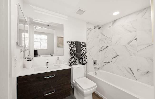a bathroom with white and black marble walls and a white tub and shower and a