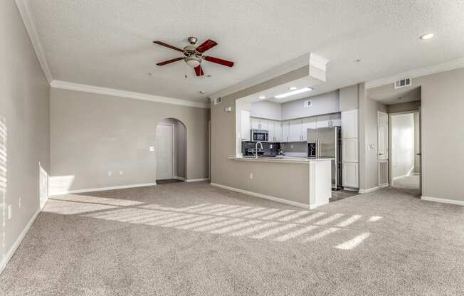 an empty living room with a ceiling fan and a kitchen