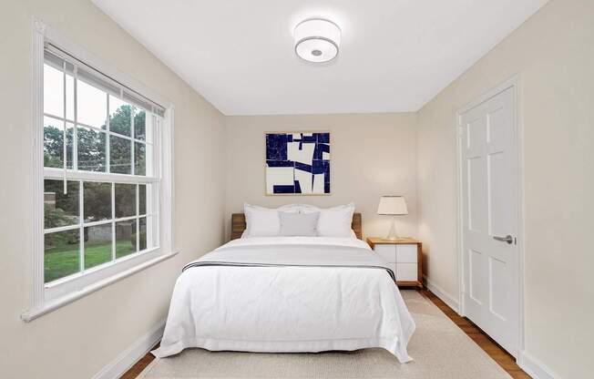 A bedroom with a large bed and a window overlooking a green lawn.