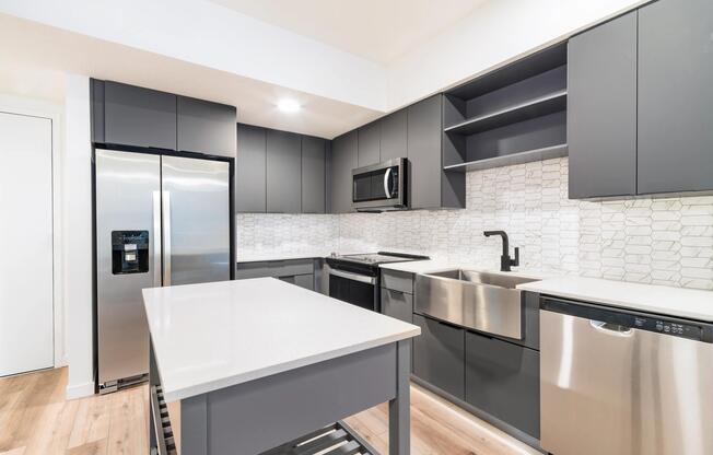 Premium finish kitchen with charcoal cabinetry, quartz countertops, a workstation sink, matte black fixtures, and stainless steel appliances.
