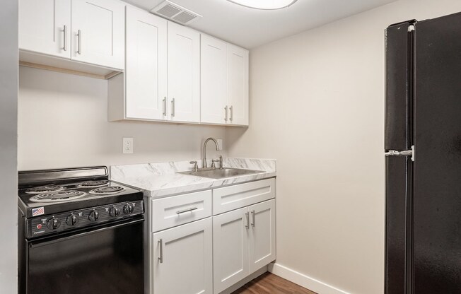 an empty kitchen with white cabinets and a black refrigerator