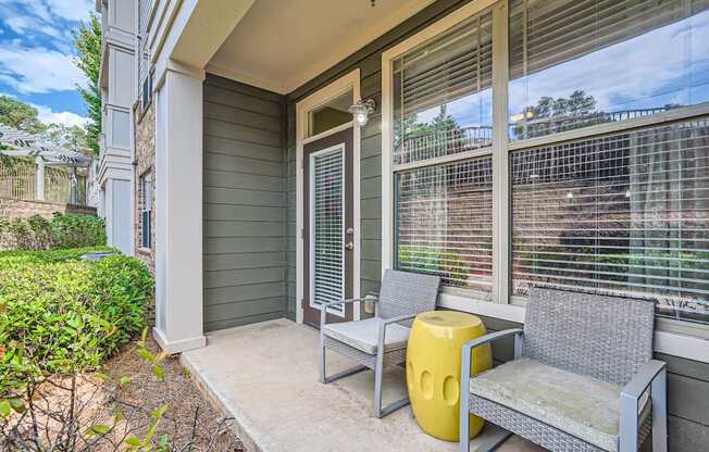 A grey wicker chair and a yellow stool are placed on a porch.