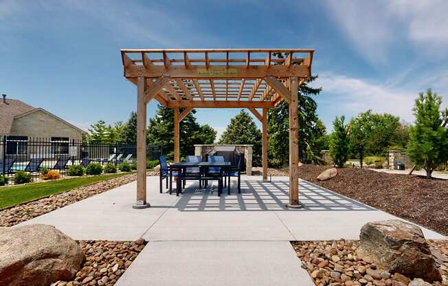 a gazebo with a table and chairs under a wooden pergola