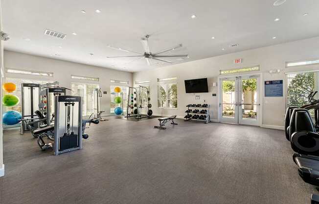 A spacious gym with a variety of equipment and a ceiling fan.